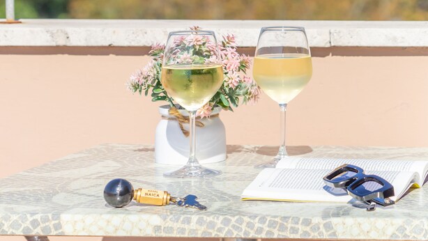 A table with a bottle of Naica champagne, two glasses of champagne, a book, and a pair of sunglasses on a balcony overlooking the sea. - HOTEL NAICA (Rimini)