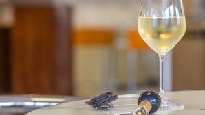 A glass of white wine on a marble table with a corkscrew and a bottle cap nearby. - HOTEL NAICA (Rimini)