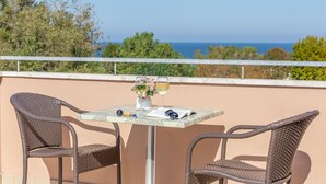 A balcony with two wicker chairs, a table, a vase with flowers, and two glasses of wine. - HOTEL NAICA (Rimini)