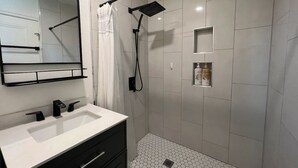 A modern bathroom with a white sink, black faucets, a mirror, a shower with a handheld showerhead, and a tiled floor. - Open concept modern home: about 20 minutes or less to Disney,Malls, Beaches, etc (Santa Ana)