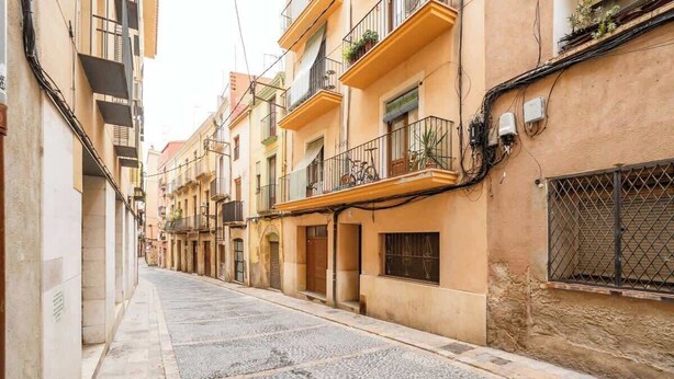 A narrow street with buildings on both sides, balconies with plants, and a cobblestone street. - Old Town • Santes Creus - Unik Vacation (Tarragona)