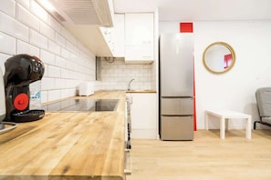 A compact kitchen with white cabinets, a stainless steel refrigerator, a coffee machine, and a small white table.
