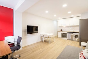 A compact living space with a dining area, kitchenette, and a TV mounted on the wall.