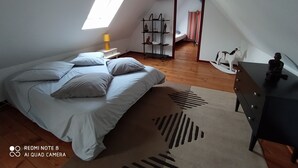 Ein Schlafzimmer mit einem Bett, einem Nachttisch, einer Kommode, einem Regal mit Figuren, einem Fenster und einer geneigten Decke.