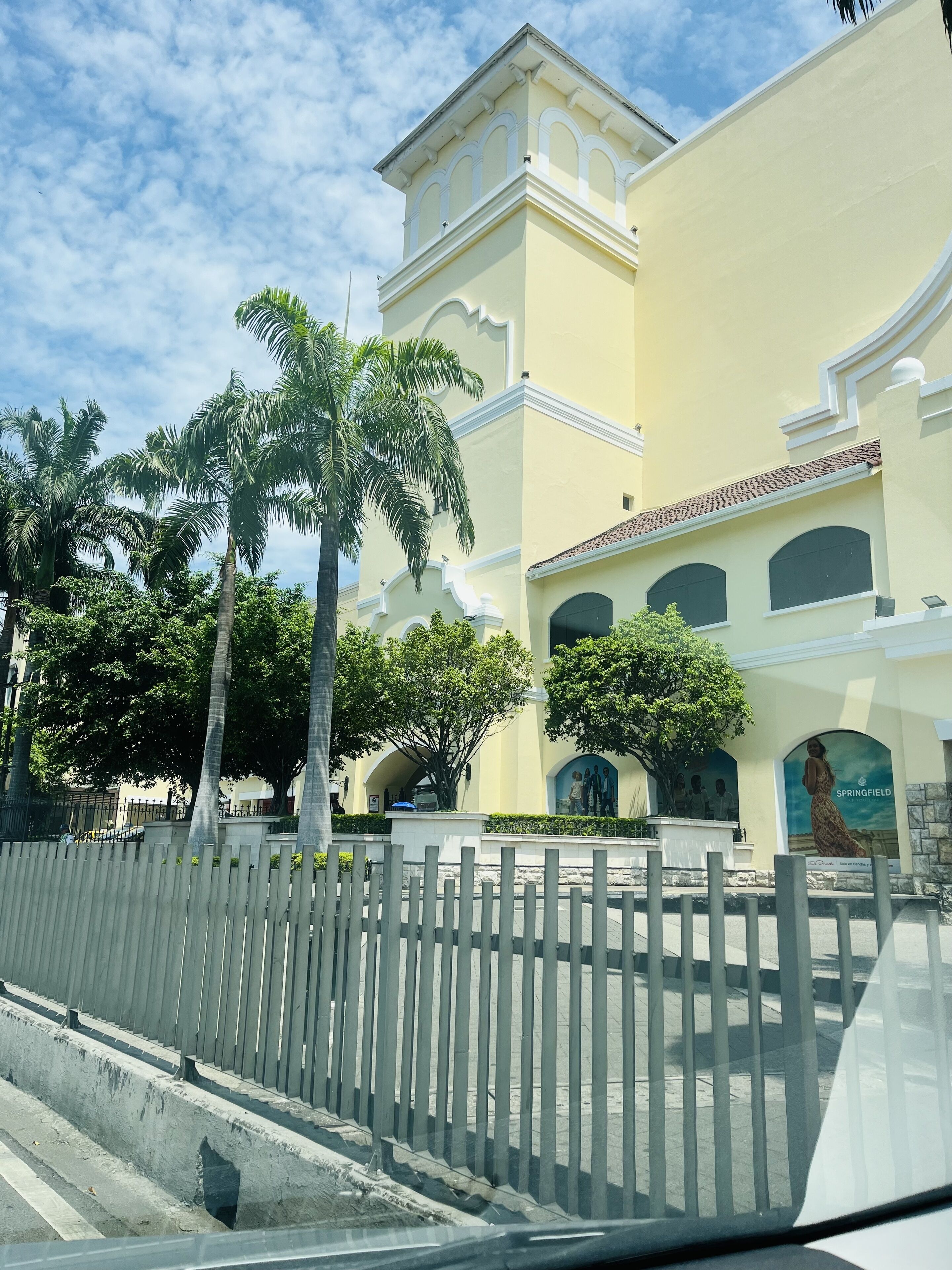 A yellow building with a white fence, palm trees, and a mural on the wall.