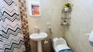 Un baño con cortina de ducha de estampado en zigzag, un lavamanos pedestal blanco, un inodoro con etiqueta 'Sanitizado', un espejo y un estante con artículos de aseo.