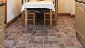 Een keuken met een houten tafel en stoelen, een betegelde vloer en houten keukenkastjes.