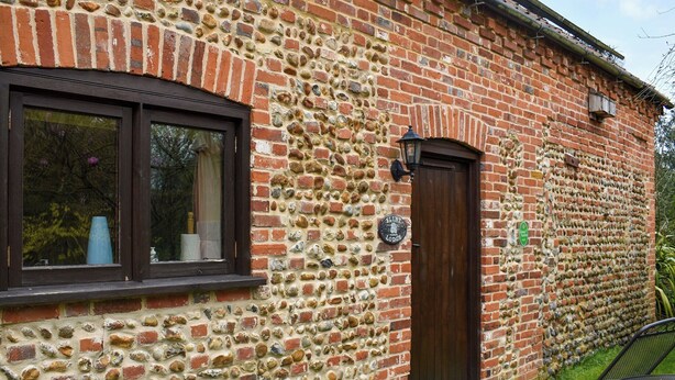 Een stenen gebouw met een donkerbruine deur en een raam met een wit object op de vensterbank.