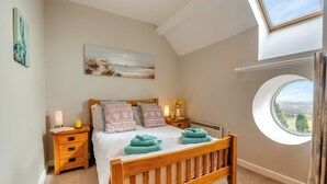 Un dormitorio con una cama de madera, un tragaluz, un ventanal redondo y un cuadro en la pared.
