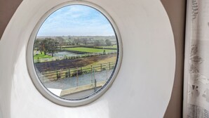 Una ventana redonda con vistas a un paisaje verde, incluyendo campos y árboles.