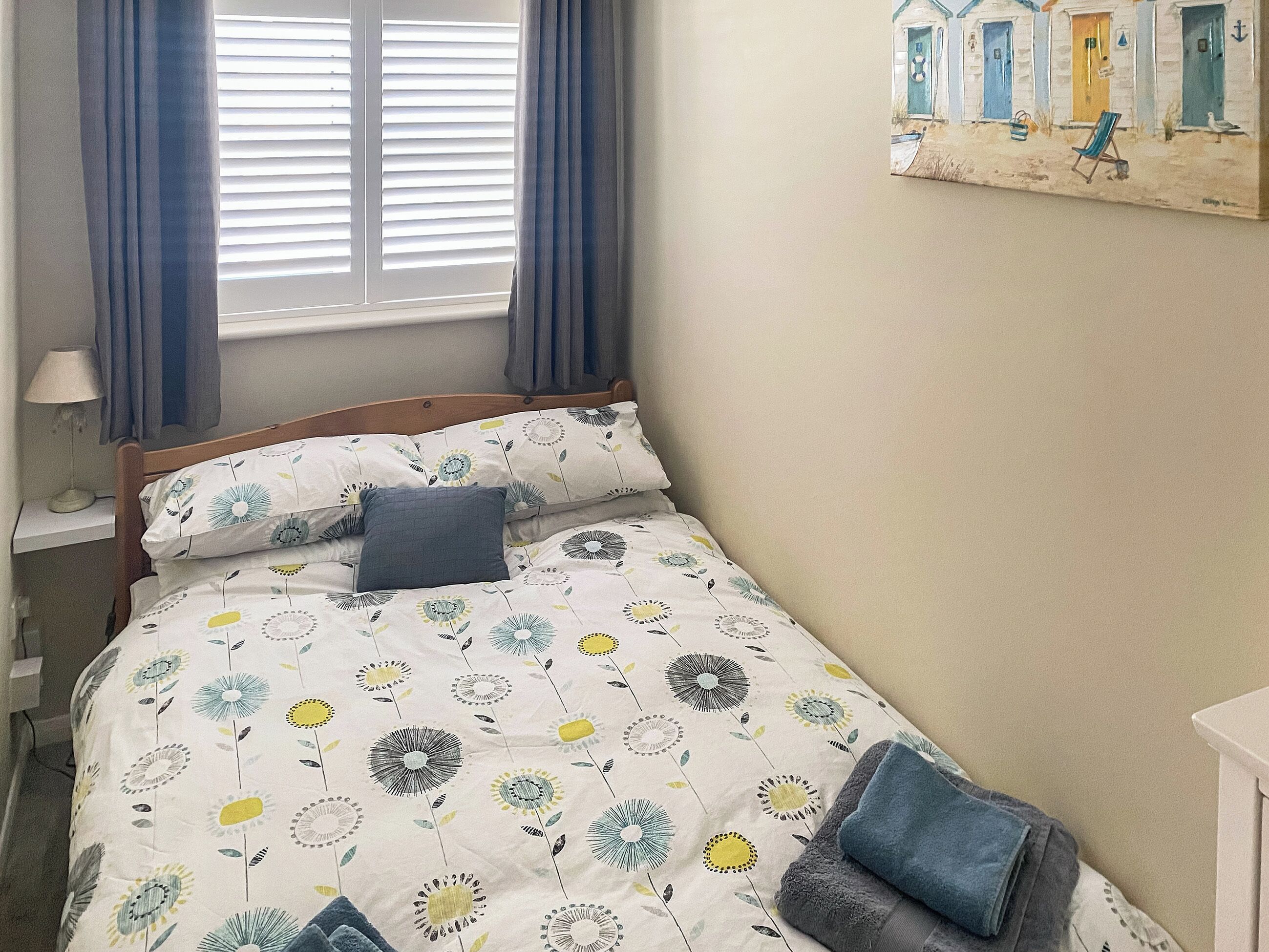 A bedroom with a bed, a nightstand, a lamp, and a painting on the wall.