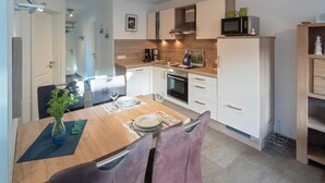 A modern kitchen with white cabinets, a wooden countertop, and a dining area with a table set for two. - Ferienwohnung Kleine Auszeit (Norddeich)