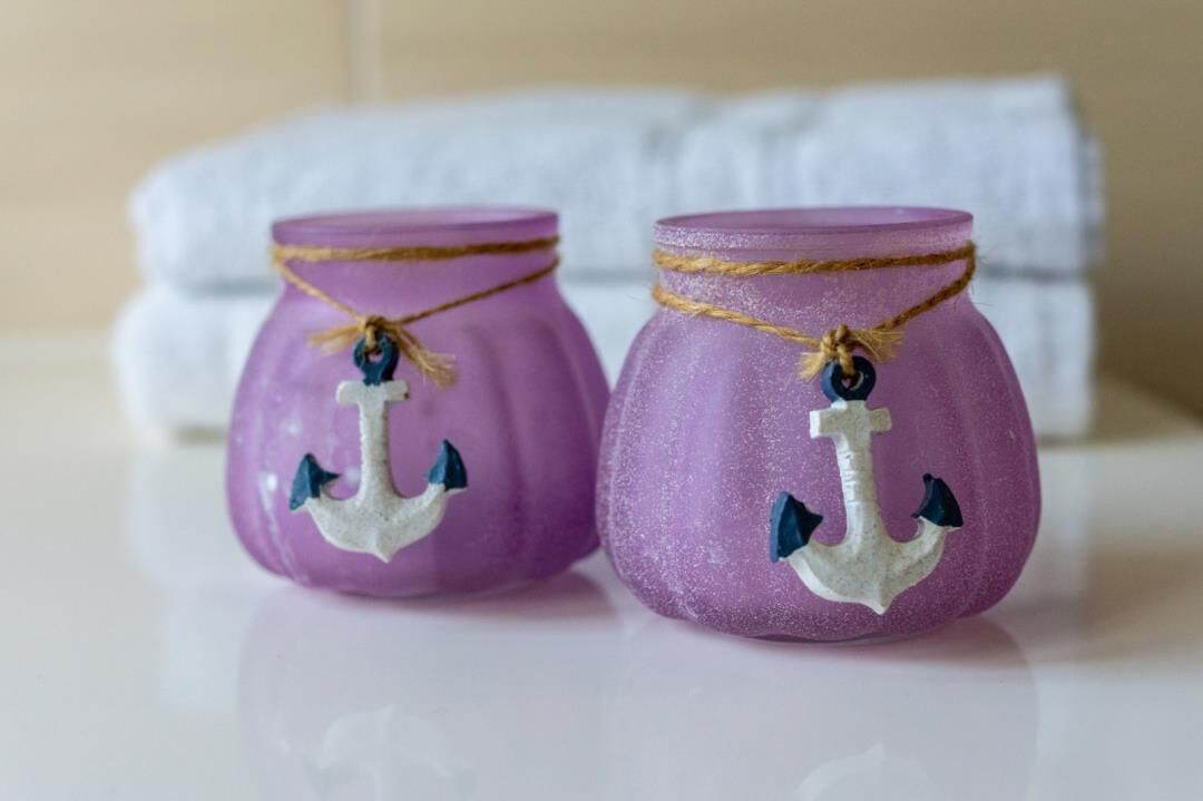 Deux pots violets décorés d’ancres et ornés de ficelle, placés sur une surface avec une serviette blanche en arrière-plan.
