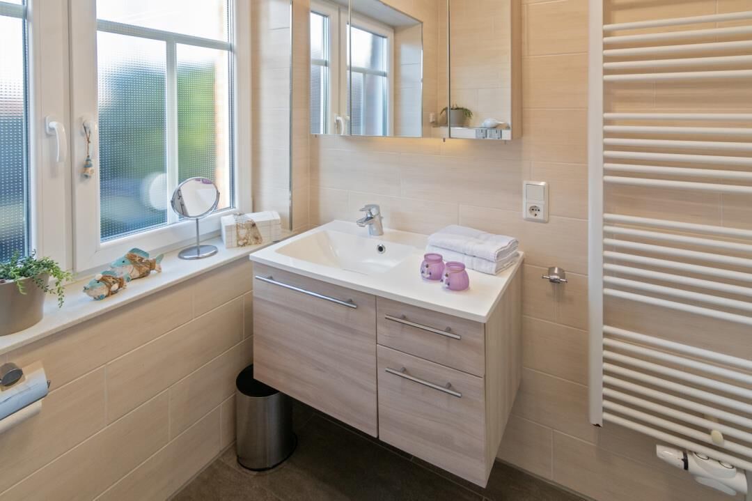 A modern bathroom with a white sink, mirror, and towel rack.