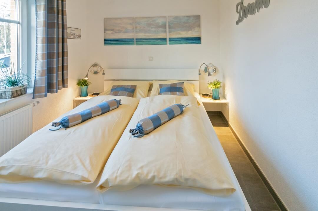 Un lit double avec des oreillers assortis et une couverture à rayures, une table de chevet avec une lampe, une fenêtre avec des rideaux et une œuvre d’art accrochée au mur.
