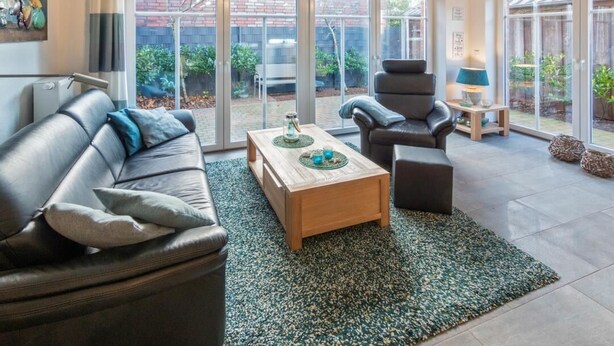 A modern living room with a leather sofa, a wooden coffee table, and a black armchair. - Ferienwohnung Kleine Auszeit (Norddeich)