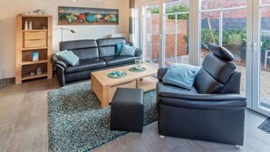 A modern living room with a black leather sofa, a wooden coffee table, and a bookshelf. - Ferienwohnung Kleine Auszeit (Norddeich)
