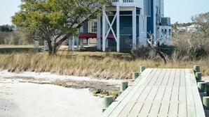 Una casa de playa de dos pisos con un balcón, un porche cubierto y una terraza de madera.