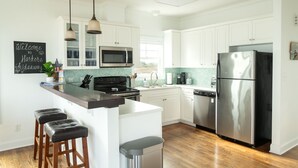 Una cocina moderna con gabinetes blancos, un refrigerador de acero inoxidable, un microondas y una isla central con taburetes.
