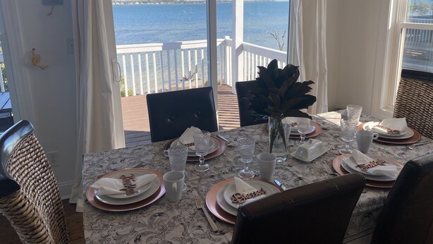 Una mesa de comedor dispuesta con platos, vasos y cubiertos, con vistas a una masa de agua.