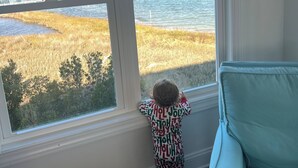 Un niño en una habitación con un amplio ventanal que da a un cuerpo de agua y un puente.