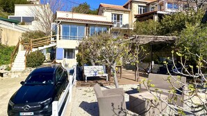 Un immeuble d’habitation avec une voiture garée devant, un escalier menant à l’entrée et du mobilier d’extérieur.