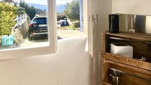 Une pièce avec un meuble en bois, une fenêtre donnant sur une voiture et sur de la verdure, et une porte blanche.