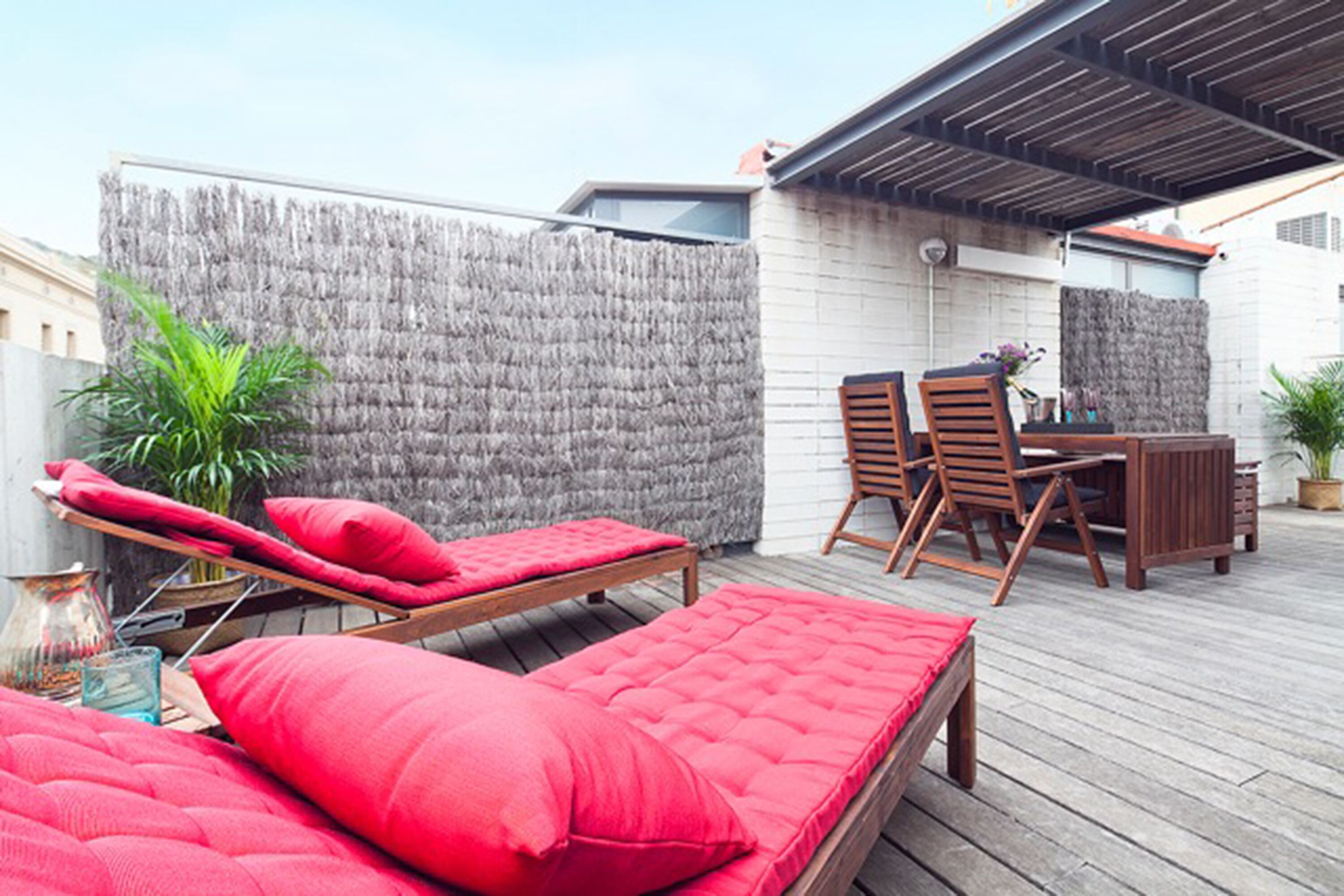 Une terrasse sur le toit avec une plateforme en bois, des sièges rembourrés de couleur rouge, une petite table et des chaises.