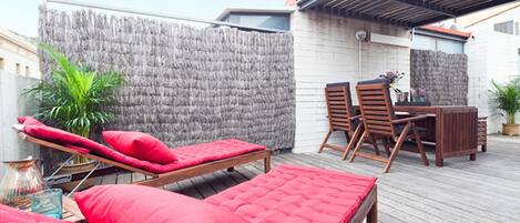 Une terrasse sur le toit avec une plateforme en bois, des sièges rembourrés de couleur rouge, une petite table et des chaises.