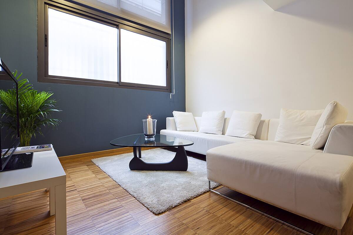 A modern living room with a white sofa, a glass coffee table, and a potted plant.
