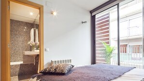 A bedroom with a large bed, a bathroom with a marble wall, and a view of a building through a window. - My Space Barcelona Park Putxet Rentals (Barcelona)