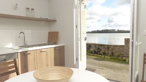 A modern kitchen with a sink, wooden cabinets, and a view of a lake through an open door.