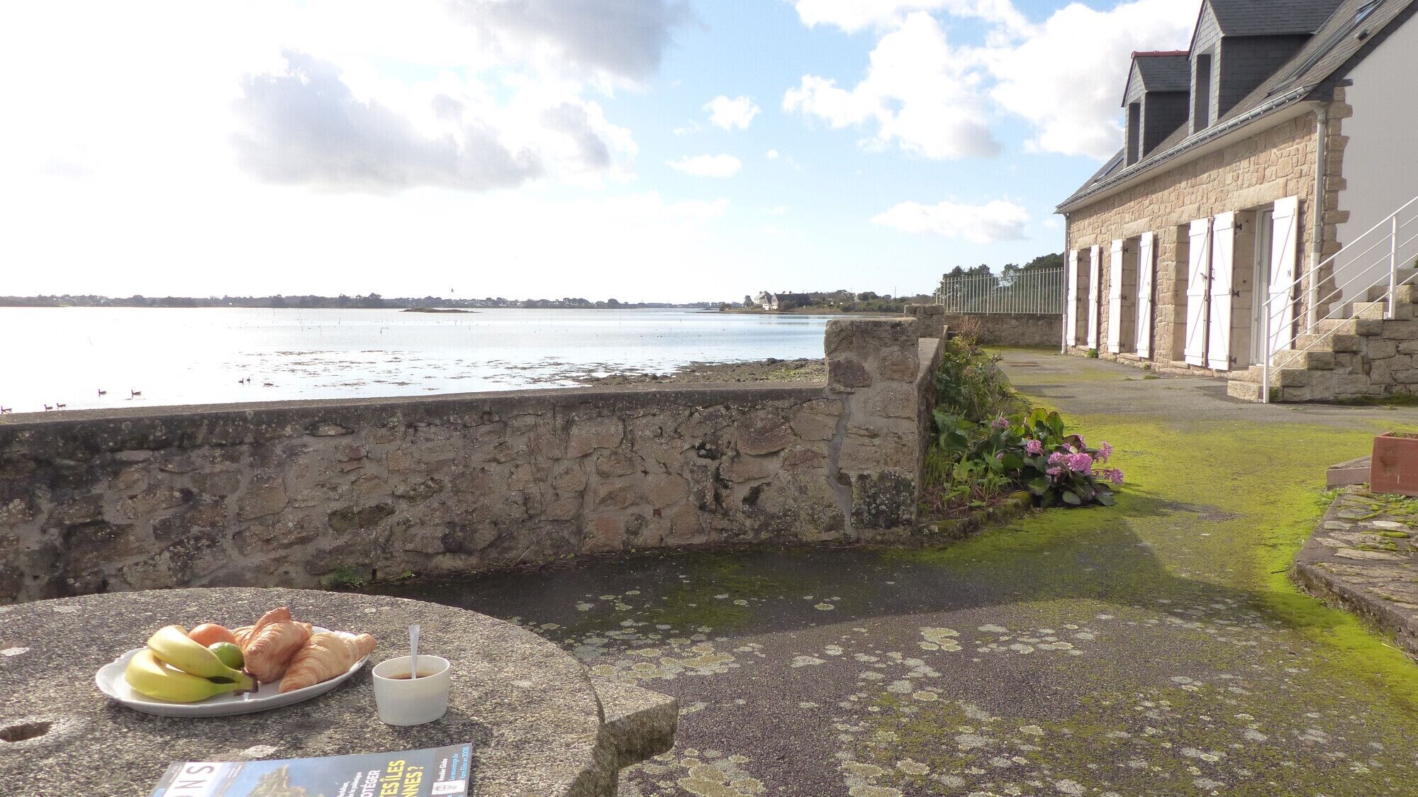 Un muro de piedra con una mesa dispuesta para una comida, con vista a un cuerpo de agua y un edificio histórico de fachada de piedra.