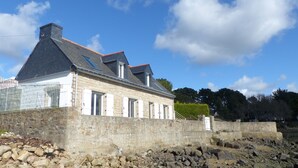 A stone building with a steep roof, multiple windows, and a stone wall foundation.