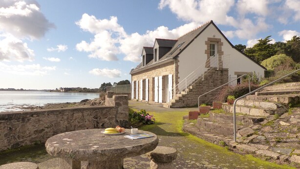 A stone building with a staircase leading to a second floor, overlooking a body of water.