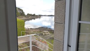 A view of a calm lake from a balcony with a stone wall and a small table and chairs.
