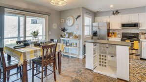 Una cocina con armarios blancos, una isla central y un comedor con mesa para cuatro.