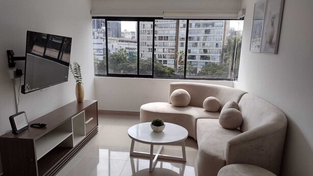 A modern living room with a sofa, a coffee table, a TV, and a large window with a city view.