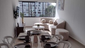 A dining area with a table set for four, a sofa, and a TV mounted on the wall.