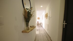 Ein schmaler Flur mit einem Holzregal, auf dem sich eine Vase mit getrockneten Pflanzen befindet, der zu einem Essbereich mit einem runden Tisch und Stühlen führt.