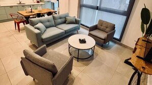 A modern living room with a sectional sofa, a round coffee table, and a small armchair. A dining area with a wooden table and chairs is visible in the background. - 207 - Apartamento Tarifa Sun (Tarifa)