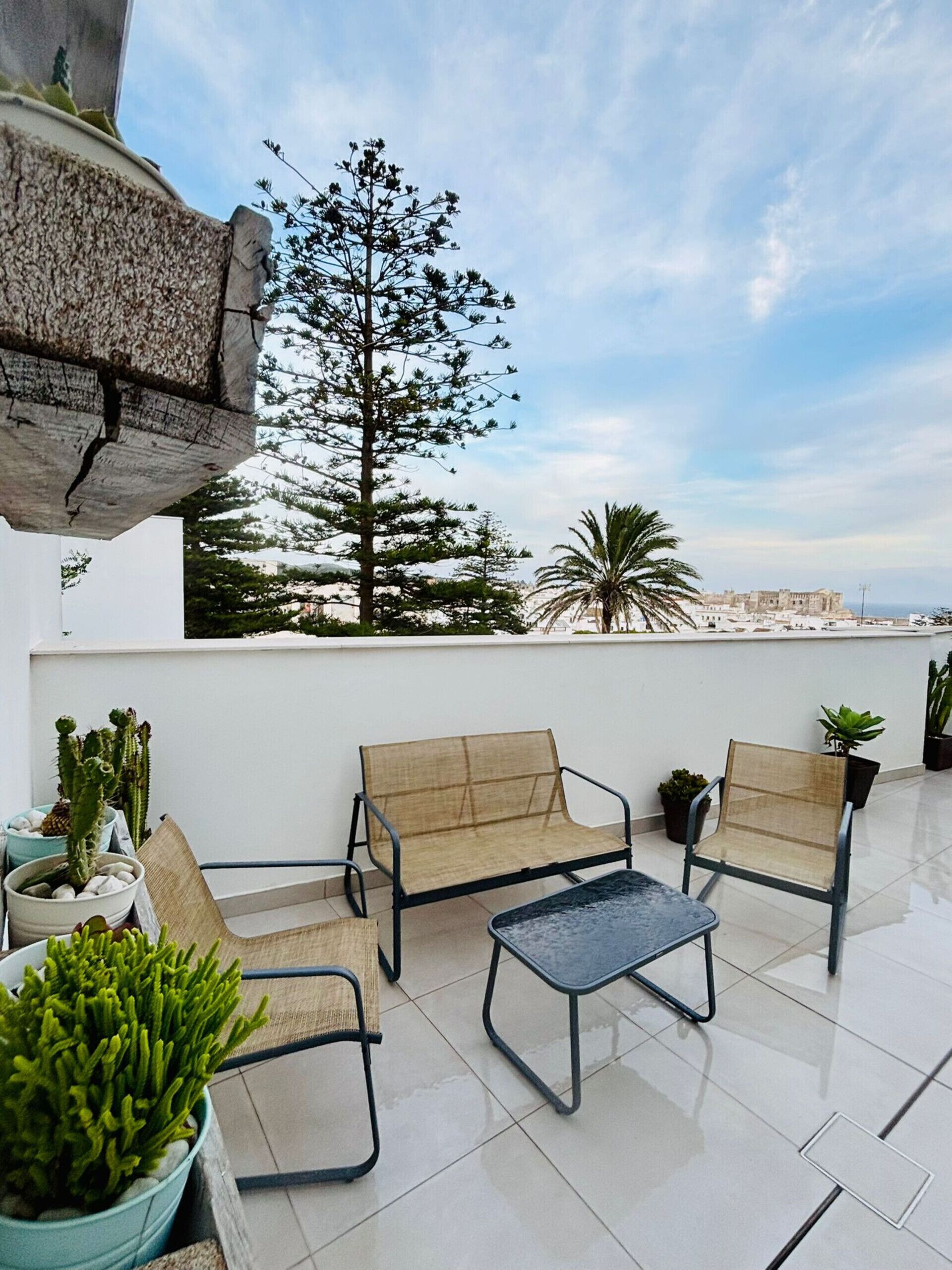 A rooftop terrace with two cushioned chairs, a small table, and potted plants.