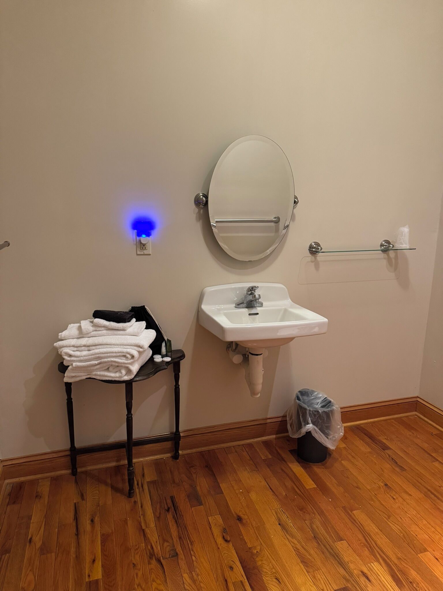 Une salle de bain avec un lavabo blanc, un miroir rond, un porte-serviettes et une petite table sur laquelle sont posées des serviettes.