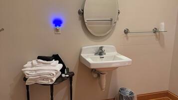 Une salle de bain avec un lavabo blanc, un miroir rond, un porte-serviettes et une petite table sur laquelle sont posées des serviettes.