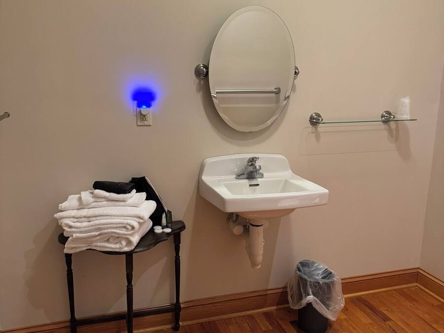 Une salle de bain avec un lavabo blanc, un miroir rond, un porte-serviettes et une petite table sur laquelle sont posées des serviettes.