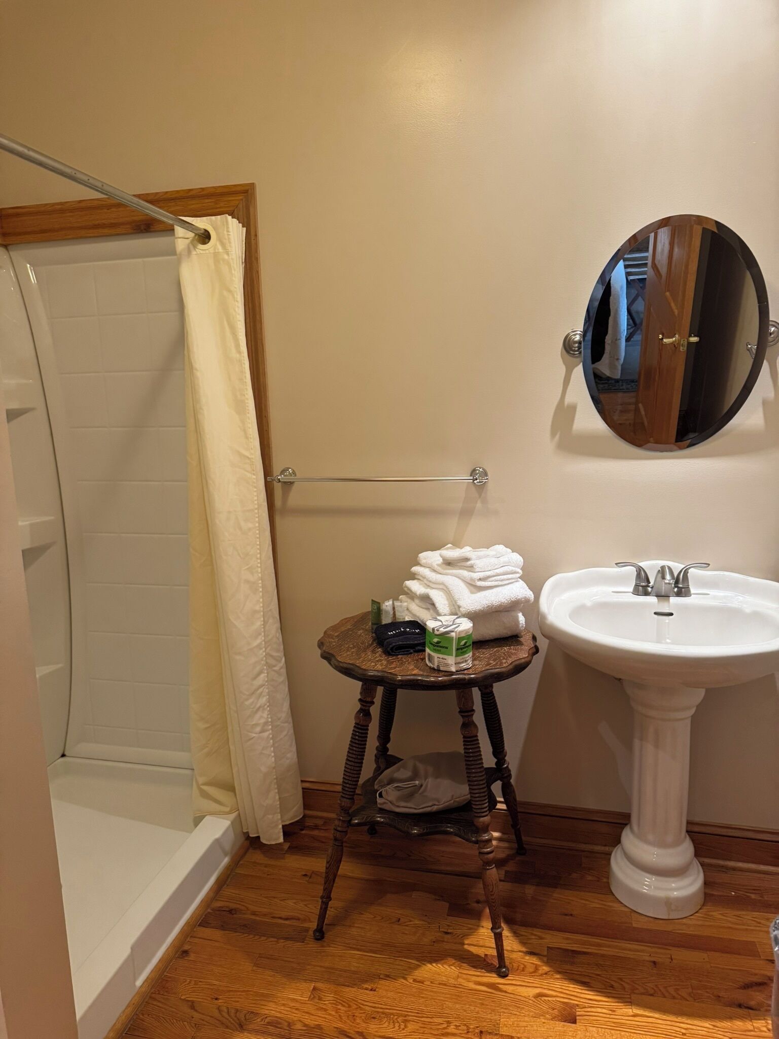 A bathroom with a shower, a sink, and a small wooden stool with towels and toiletries.