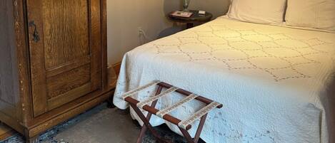 A bedroom with a wooden wardrobe, a bed with white bedding, a small table with a lamp, and a ceiling fan.