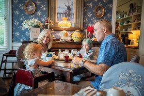 Una familia cenando en una mesa con papel tapiz floral, un candelabro y decoración vintage.