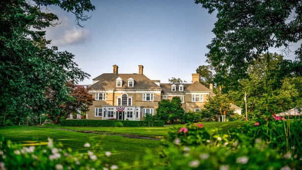 A large, historic building with a symmetrical facade, multiple chimneys, and a central entrance with a flag. - Kane Manor Inn (Kane)