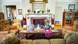 A traditional living room with patterned sofas, a fireplace, and a mirror above it. - Kane Manor Inn (Kane)